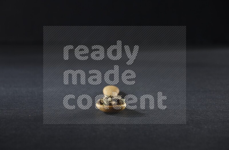 A wooden spoon full of cardamom on black flooring