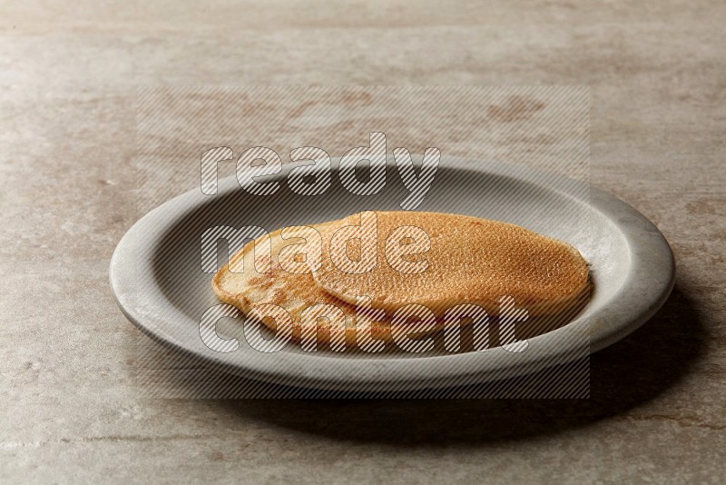 Two stacked plain pancakes in a grey plate on beige background