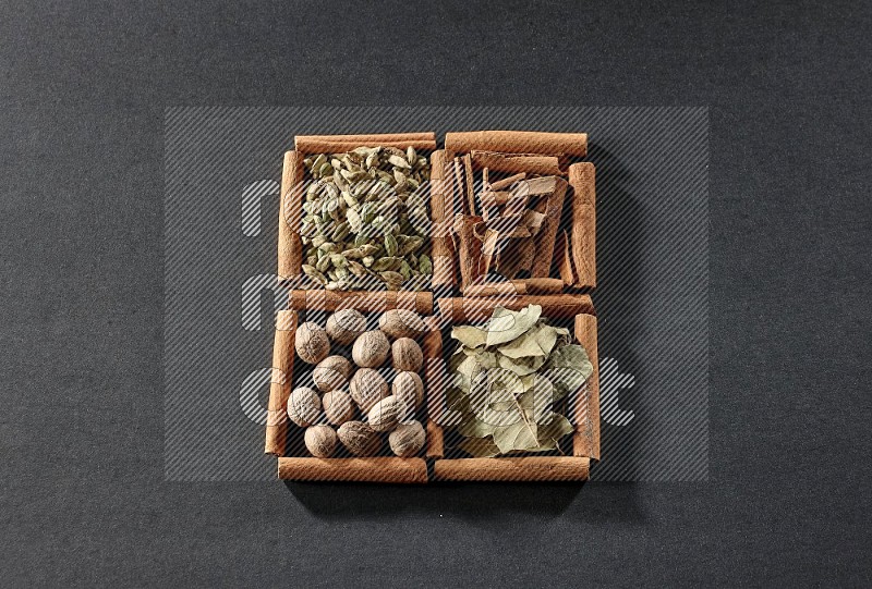 4 مربعات من عيدان القرفة ممتلئة بقطع القرفة وحبوب الهيل وأوراق الغار وجوزة الطيب على أرضية سوداء