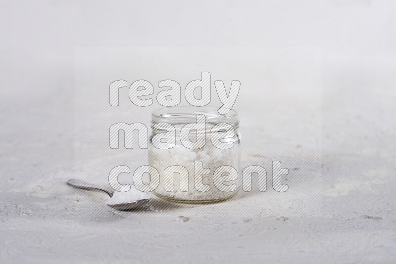 A glass jar full of coarse sea salt crystals on white background