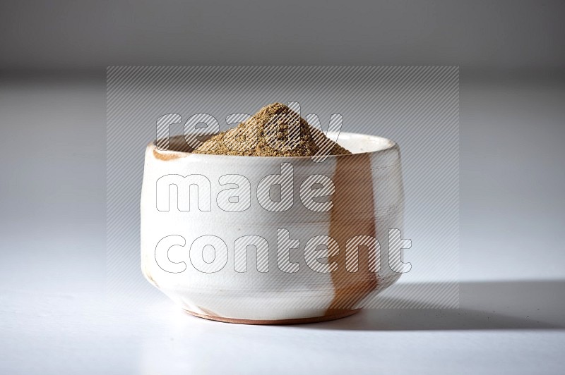 A beige bowl full of cumin powder on a white flooring