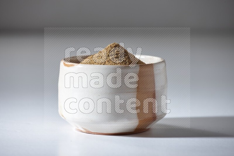 A beige bowl full of cumin powder on a white flooring