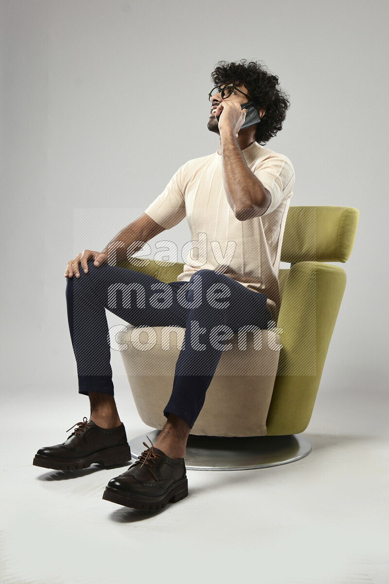 A man wearing casual sitting on a chair talking on the phone on white background