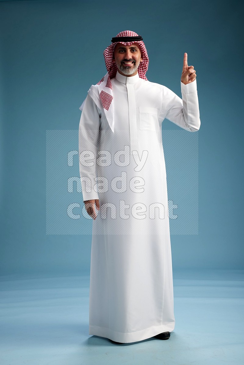 Saudi man wearing thob and shomagh posing to the camera on blue background