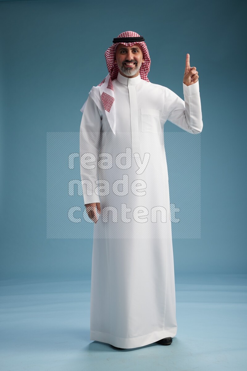 Saudi man wearing thob and shomagh posing to the camera on blue background