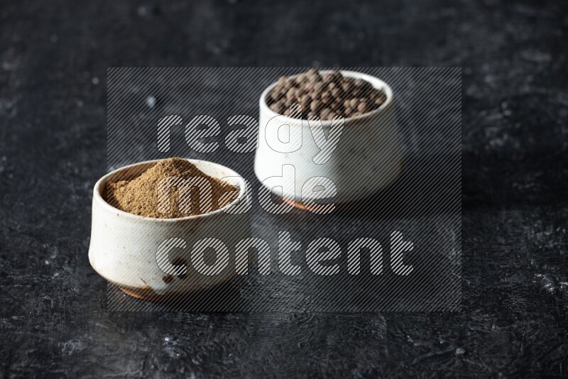 2 beige bowls, one full of allspice powder and the other full of whole balls on a textured black flooring
