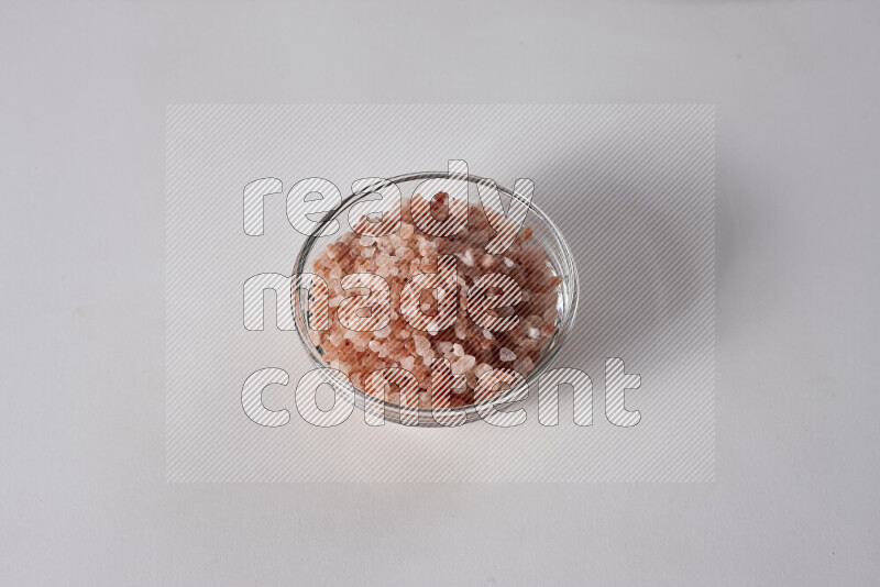 A glass bowl full of coarse himalayan salt crystals on white background