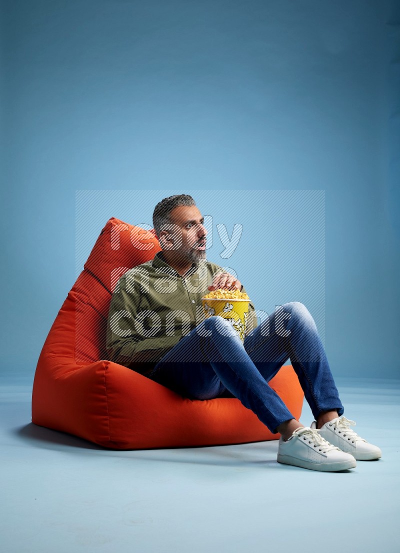 A man sitting on an orange beanbag and eating popcorn