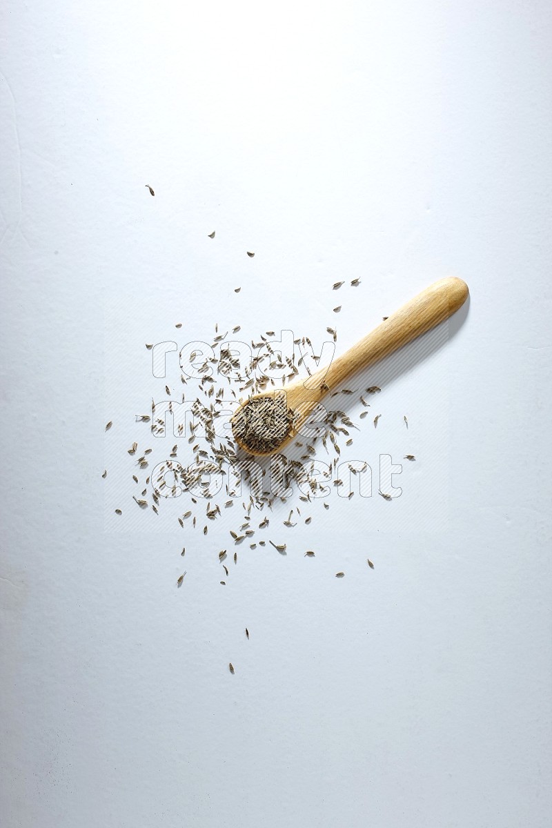 A wooden spoon full of cumin seeds on a white flooring