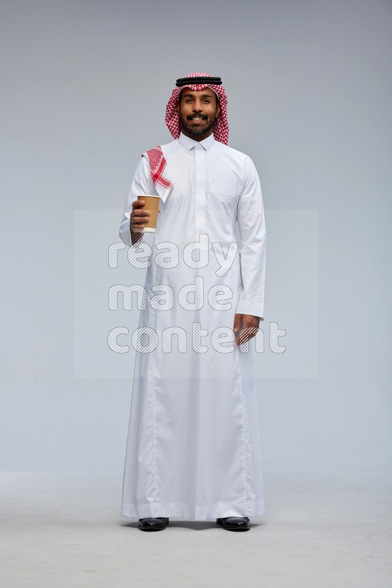 Saudi man Wearing Thob and shomag standing holding paper cup on Gray background