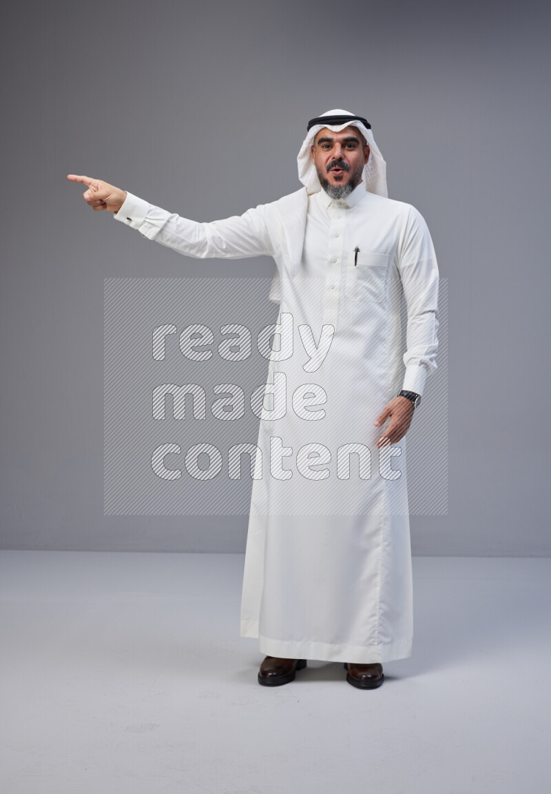 Saudi man Wearing Thob and white Shomag standing interacting with the camera on Gray background