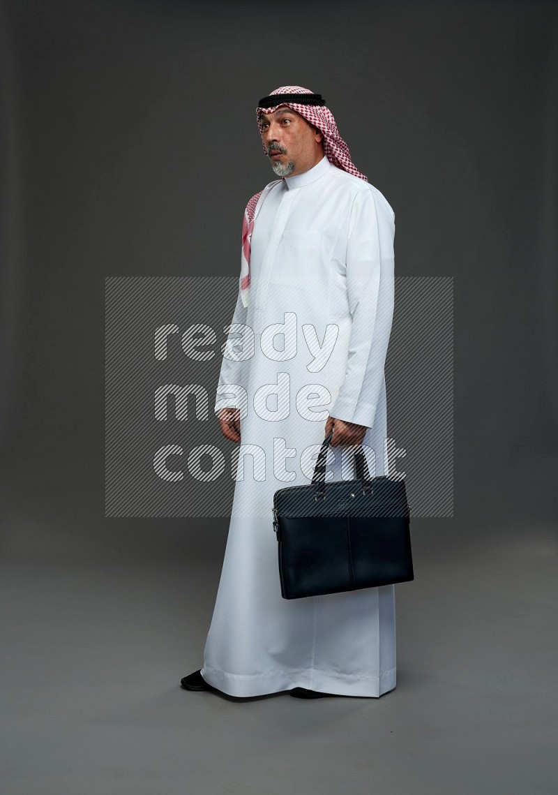 Saudi man with shomag Standing holding bag on gray background