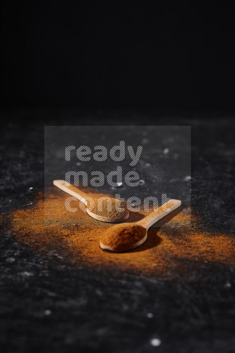 Two wooden spoons full of ground paprika powder on black background