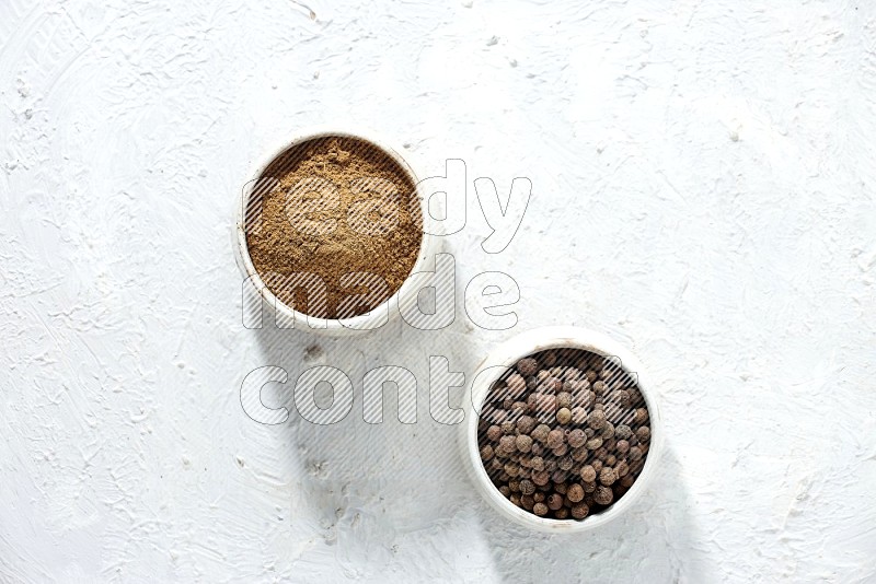 2 beige bowls, one full of allspice powder and the other full of whole balls on a textured white flooring