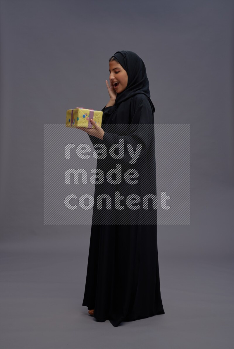 Saudi woman wearing Abaya standing holding gift box on gray background