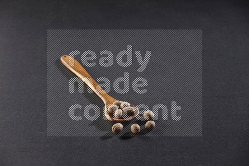 A wooden ladle full of nutmeg on a black flooring in different angles