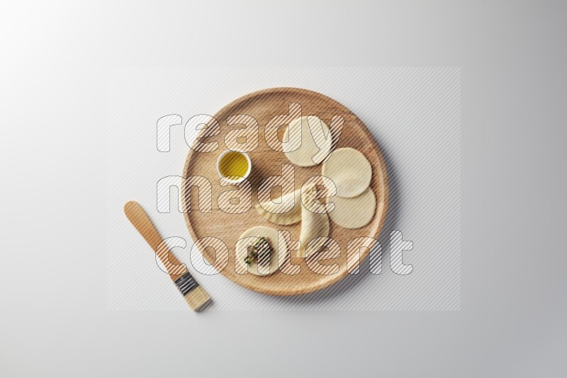 two closed sambosas and one open sambosa filled with meat while oil with oil brush aside in a wooden dish on a white background
