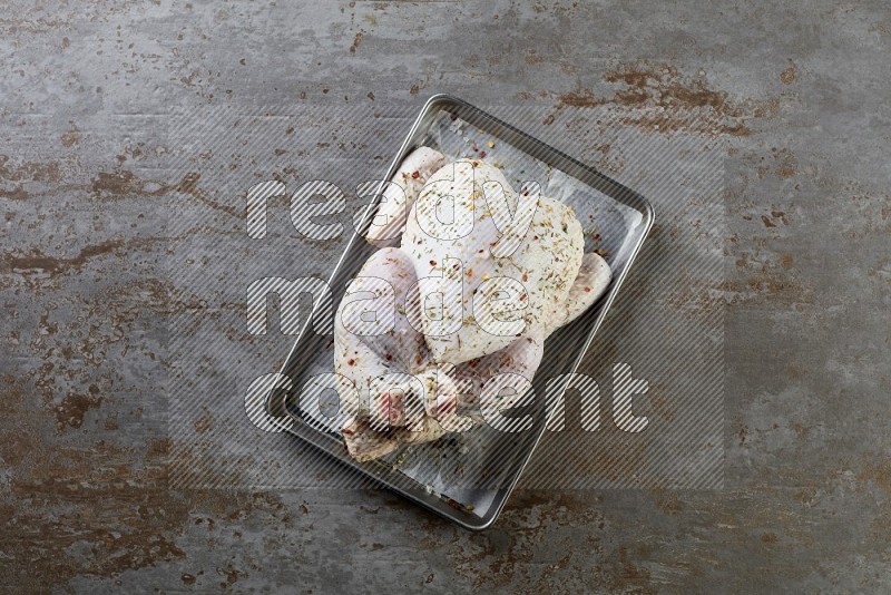 whole Raw chicken on a small oven trey direct on a rustic grey background