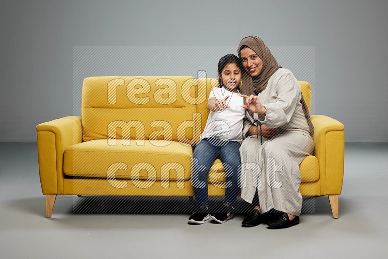 Mom and daughter sitting on sofa holding ATM card on gray background