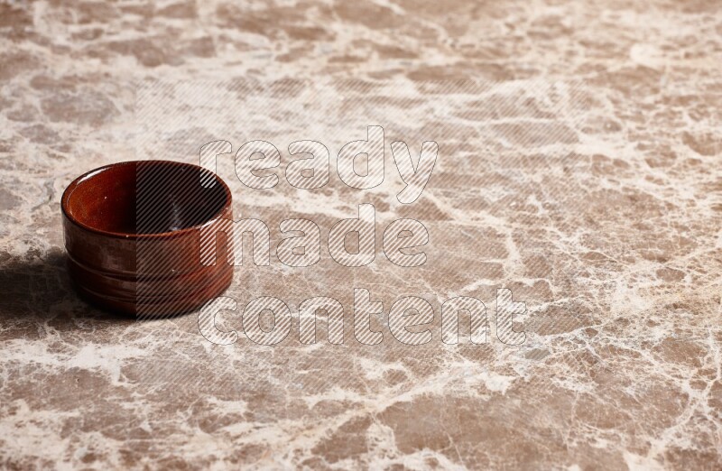 A brown pottery bowl on beige marble background