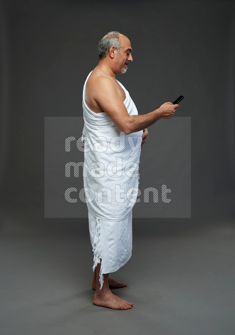 A man wearing Ehram Standing texting on phone on gray background