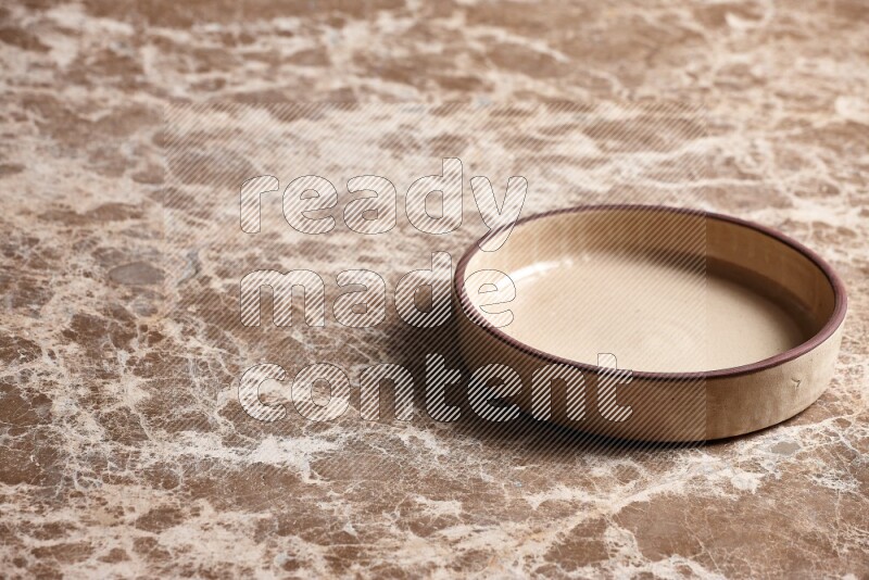 A beige pottery oven plate on beige marble background