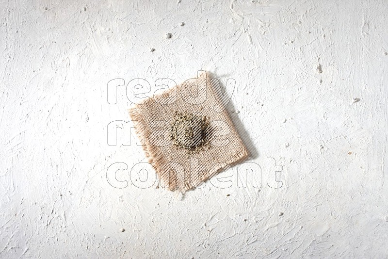 Cumin seeds on a burlap piece on a textured white flooring