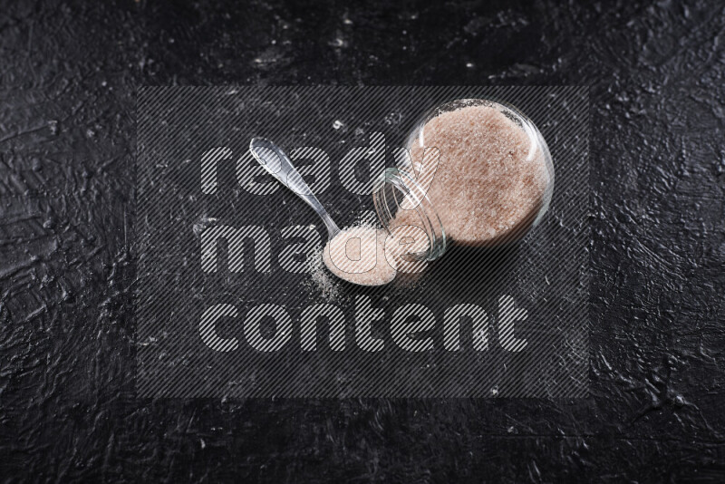 A glass jar full of fine himalayan salt on black background