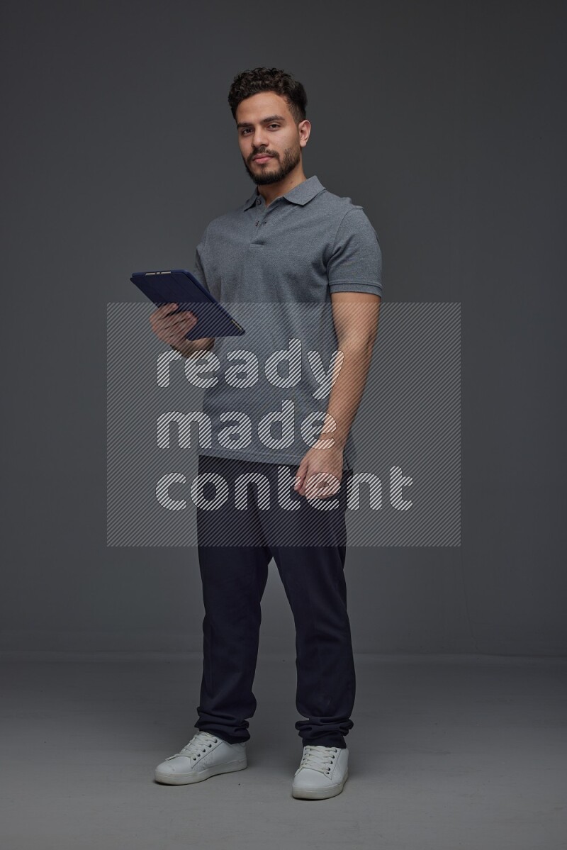 A man wearing casual standing and using his tablet and making multi hand gestures different angles eye level on a gray background