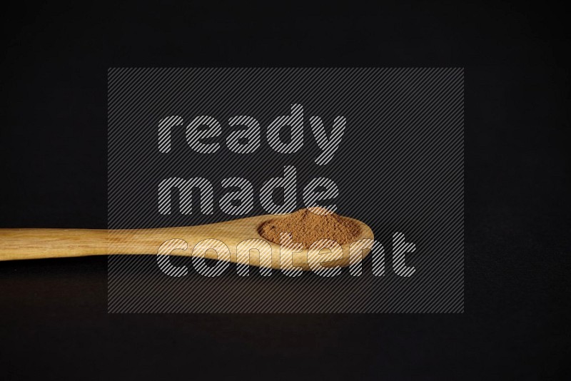 Cinnamon powder in a wooden spoon on a black background