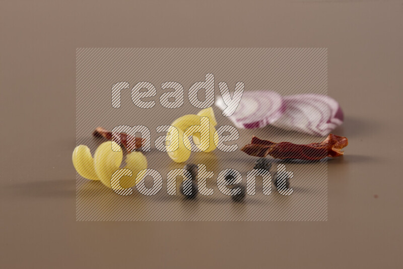 Raw pasta with different ingredients such as cherry tomatoes, garlic, onions, red chilis, black pepper, white pepper, bay laurel leaves, rosemary and cardamom on beige background