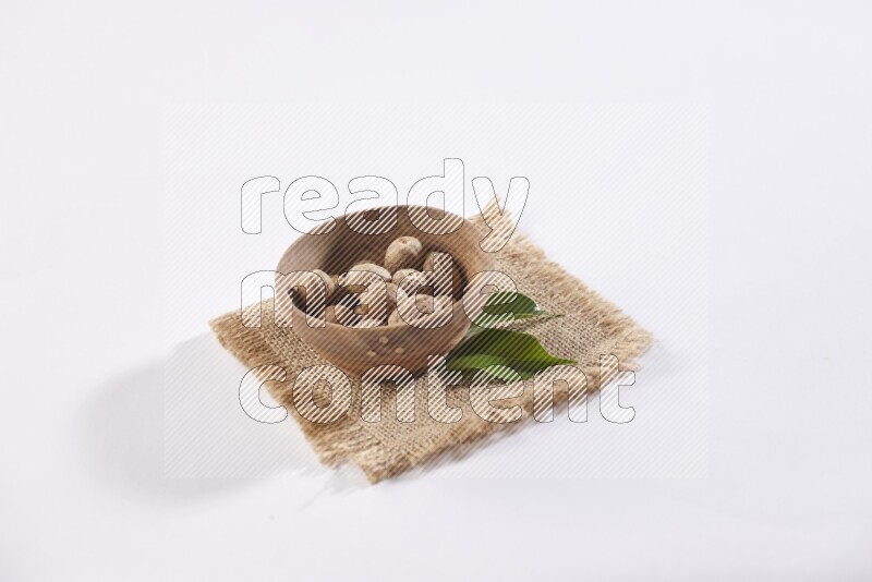 A wooden bowl full of whole nutmeg seeds on burlap fabric on a white flooring