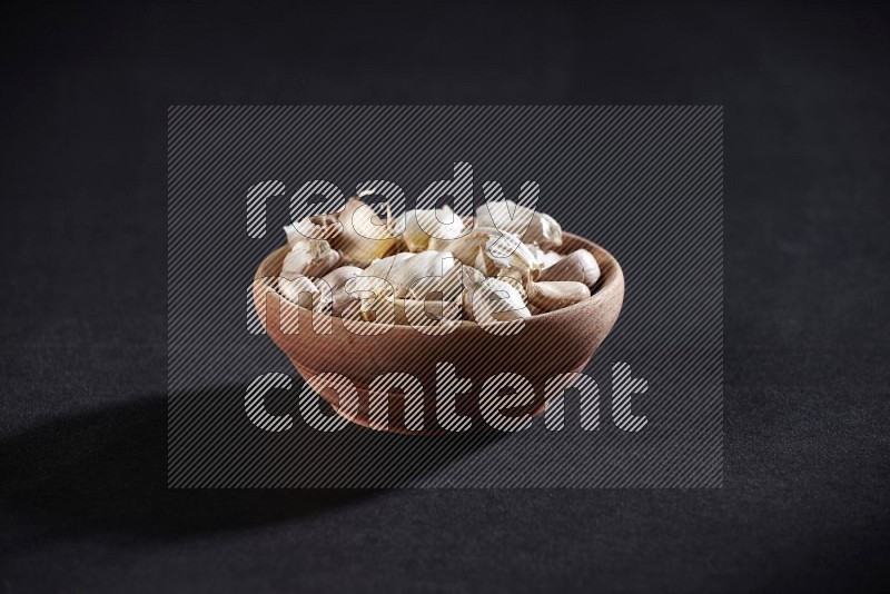 A wooden bowl full of garlic cloves on a black flooring