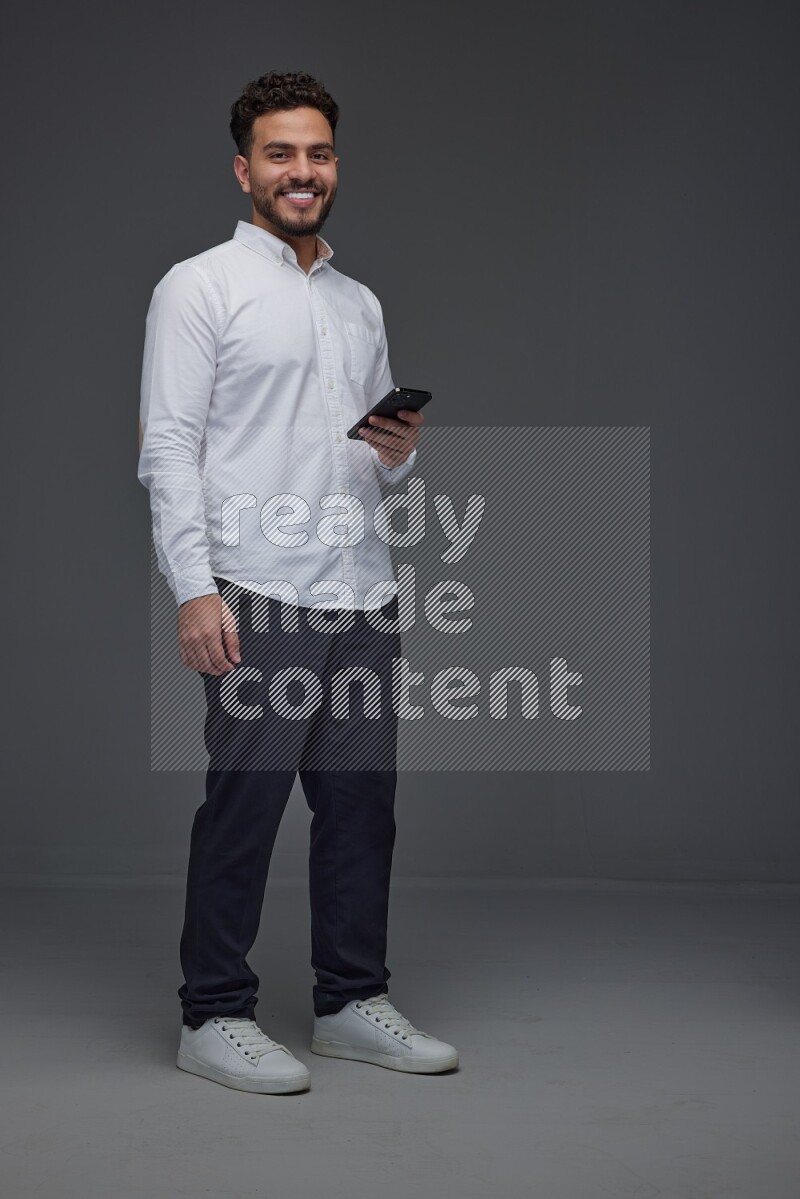 A man wearing smart casual standing and using his phone eye level on a gray background