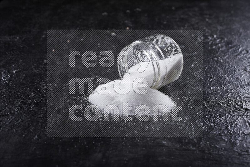 A glass jar full of fine table salt on black background