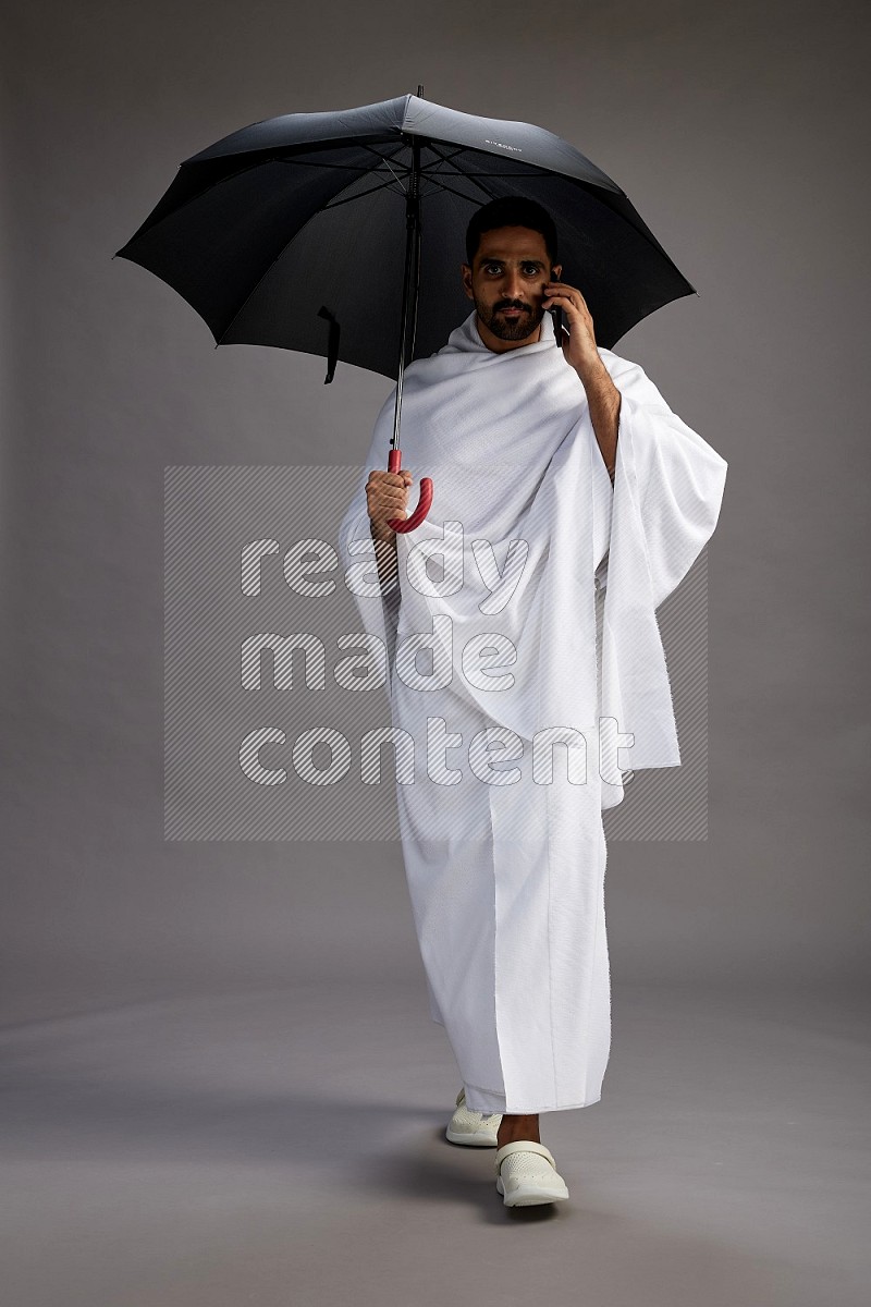 A man wearing Ehram Standing holding umbrella on gray background