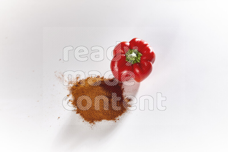 A bunch of ground paprika powder with a red bell pepper beside it on white background