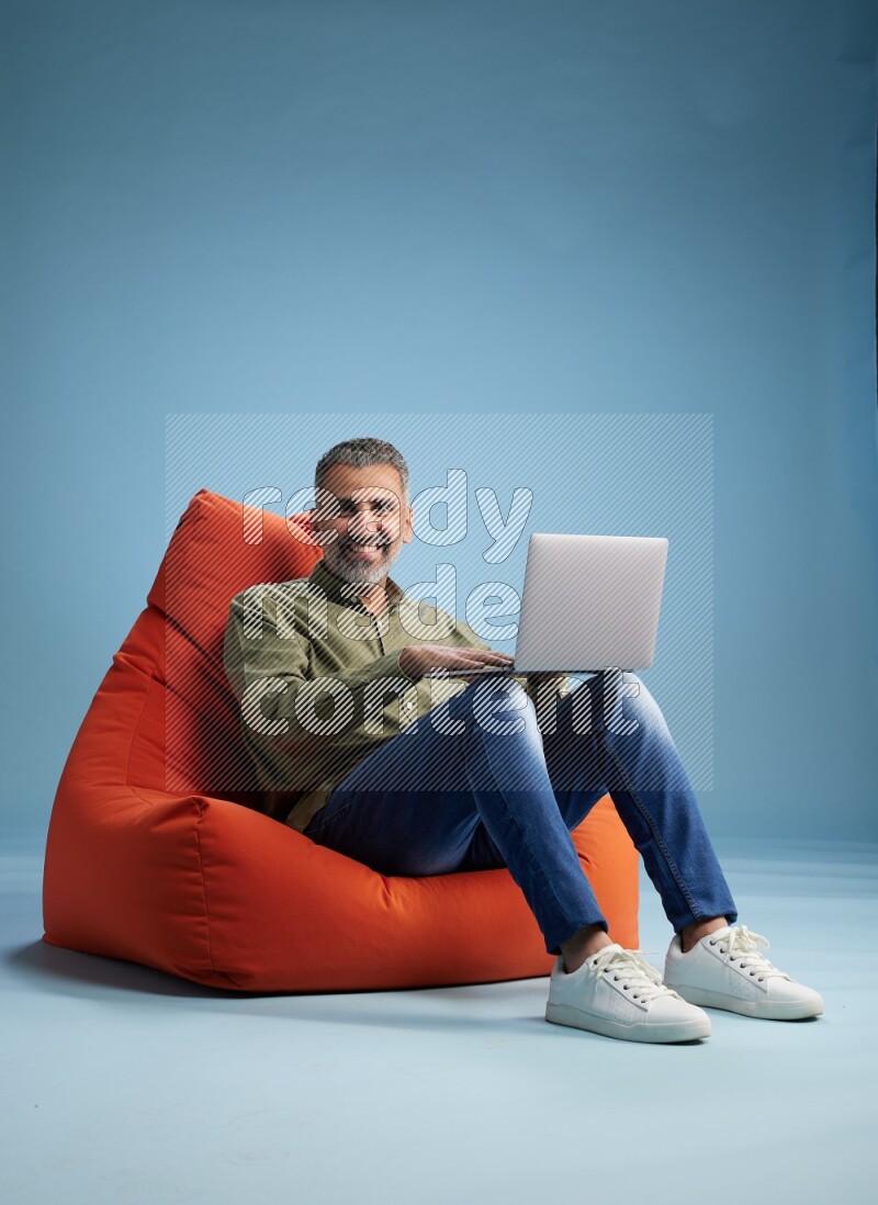 A man sitting on an orange beanbag and working on laptop