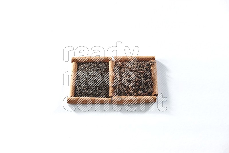 مربعان من أعواد القرفة ممتلئان بالشاي الأسود وحبوب القرنفل علي خلفية بيضاء