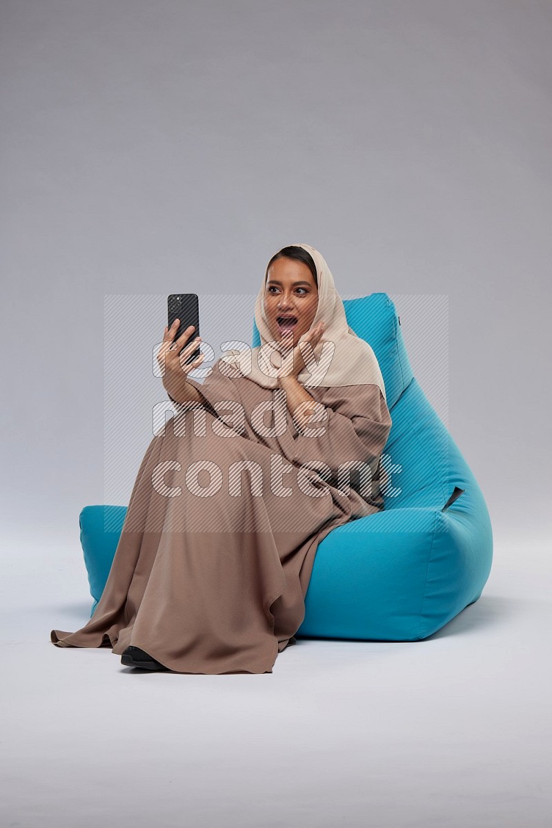A Saudi woman sitting on a blue beanbag and taking selfie