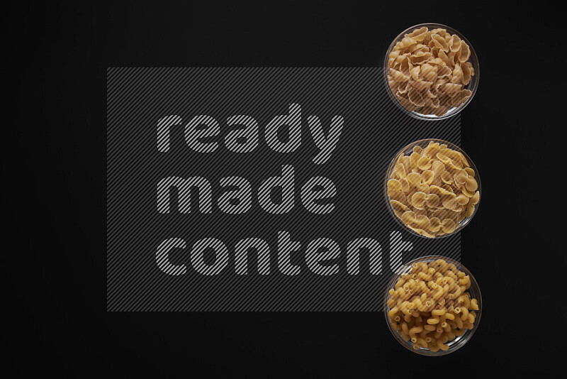 Different pasta types in 3 glass bowls on black background