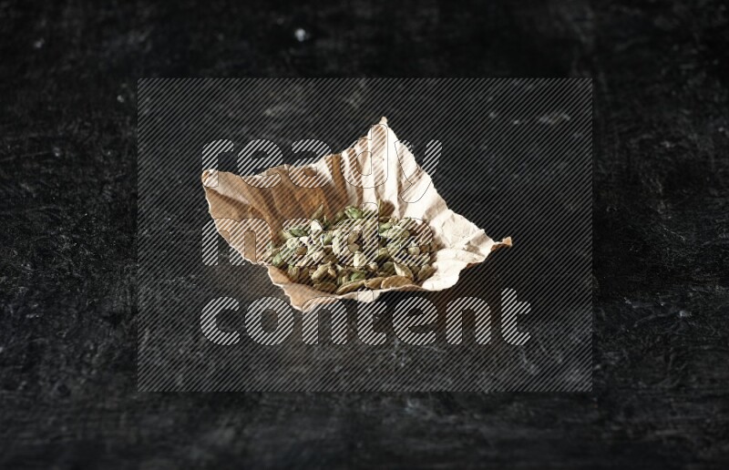 Cardamom seeds in a crumpled piece of paper on textured black flooring