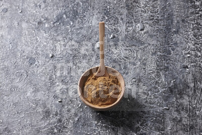 Wooden bowl full of cinnamon powder with a wooden spoon on a textured black background in different angles