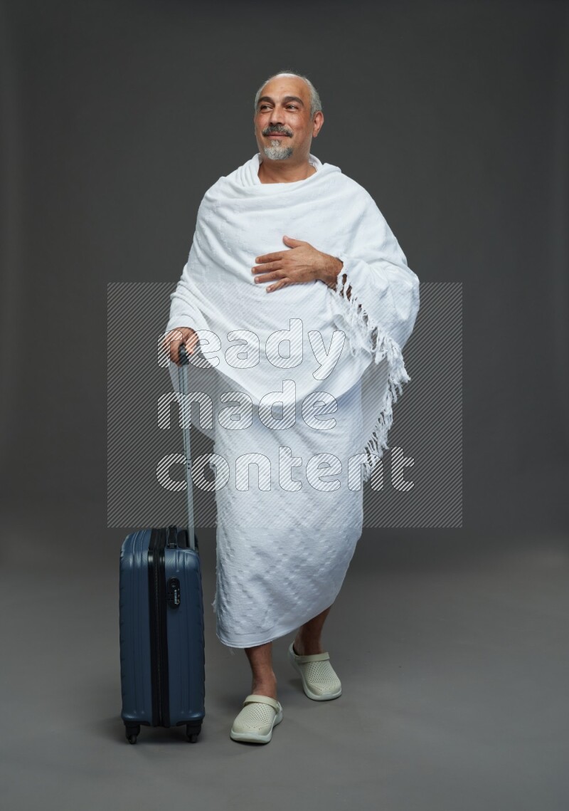 A man wearing Ehram Standing holding traveling bag on gray background