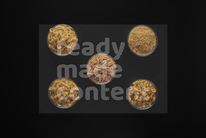Different pasta types in 5 glass bowls on black background