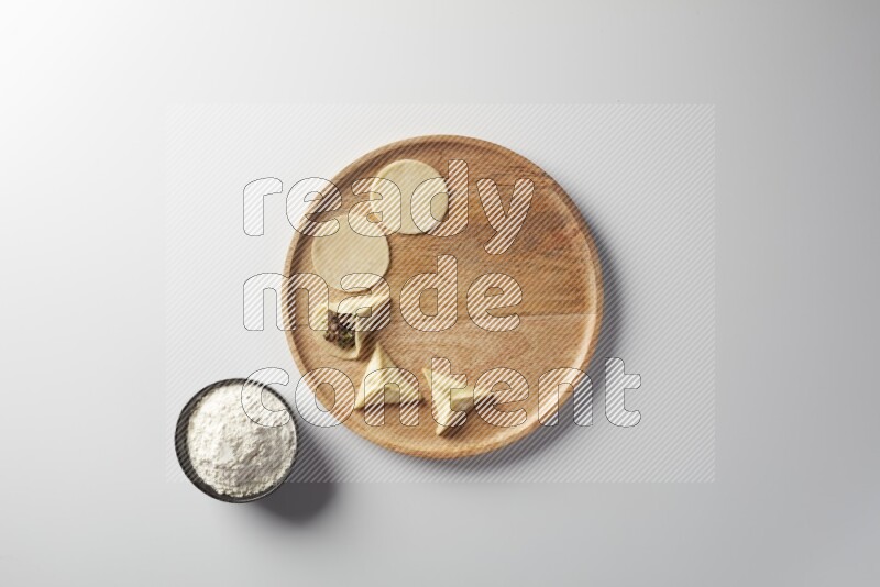 two closed sambosas and one open sambosa filled with meat while flour aside in a wooden dish on a white background