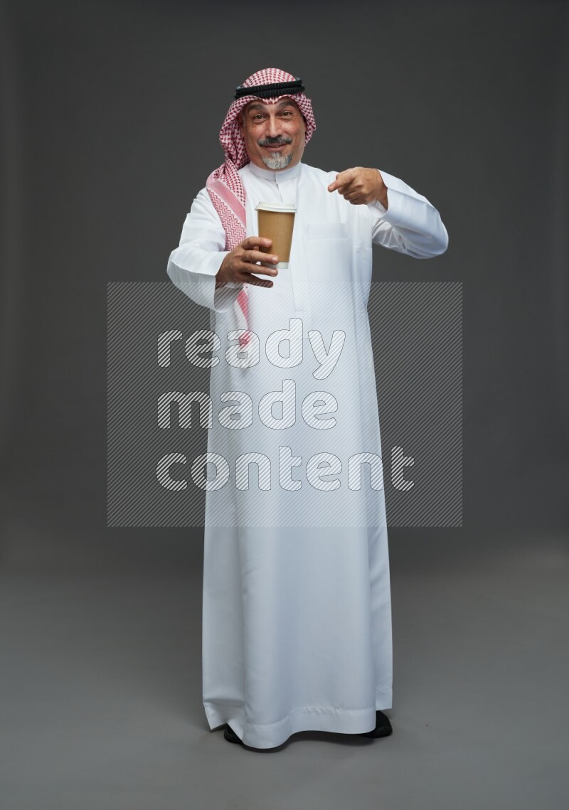 Saudi man with shomag Standing holding paper cup on gray background