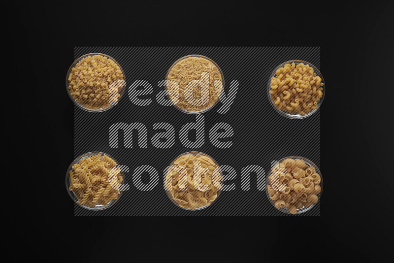 Different pasta types in 6 glass bowls on black background