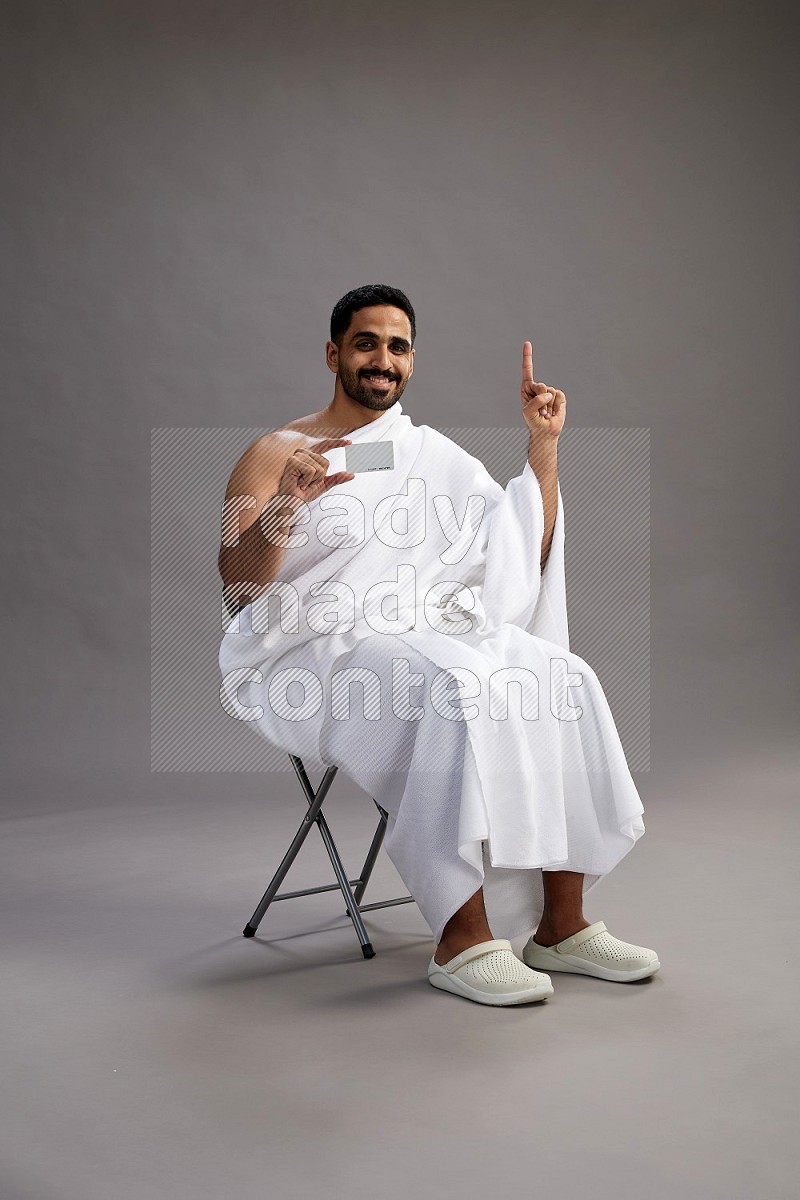 A man wearing Ehram sitting on chair holding ATM card on gray background