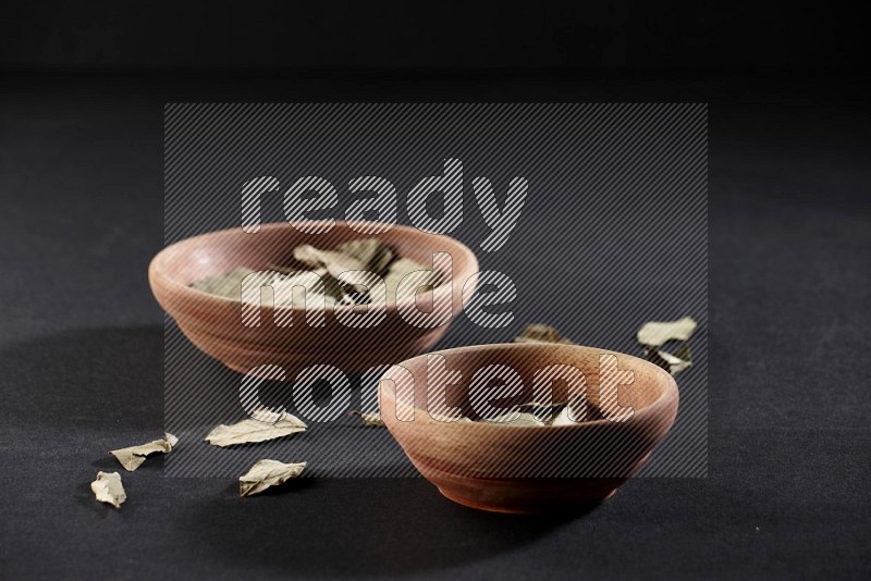 2 wooden bowls filled with laurel bay on black flooring in different angles